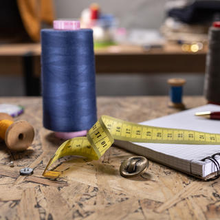 Mesa de ateliê de costura com carretel de linha, botões, caderno de anotações e fita métrica