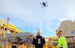 Imagem de dois colaboradores uniformizados do Bureau Veritas olhando para um drone voando por um site industrial