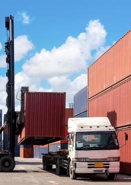 doca com containers empilhados, com um homem parado perto de um caminhão que será carregado com um desses containers
