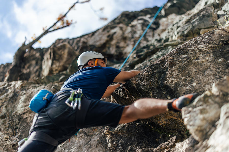 Homem escalando parede de pedra com equipamentos de segurança